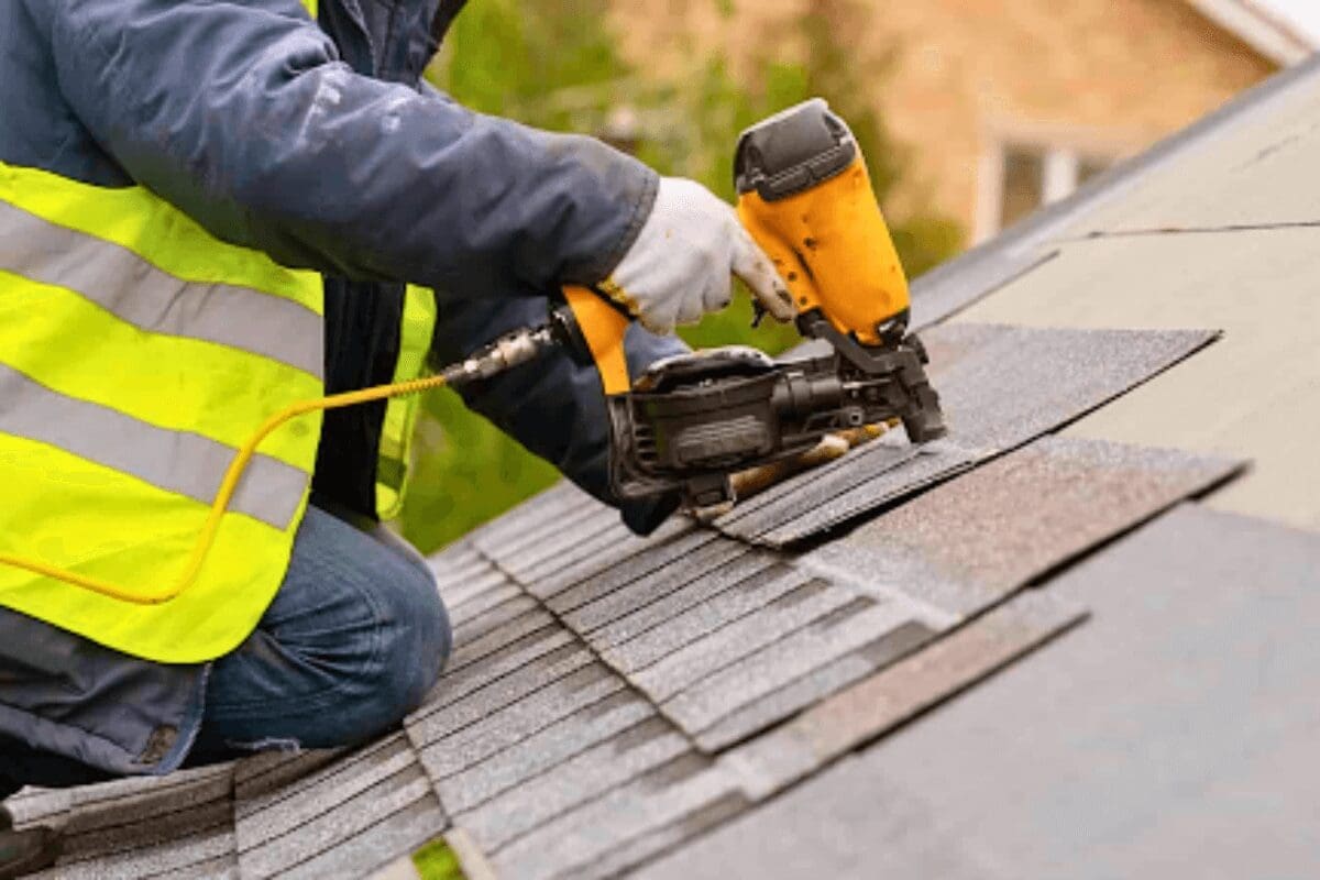 Man in construction vest kneeling on roof layering shingles