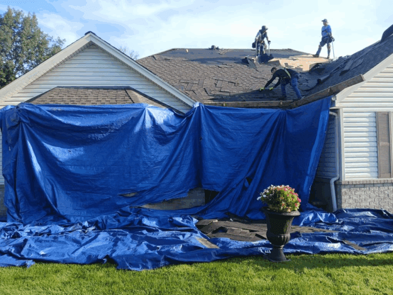 Modern Exterior tearing off old hail-damaged shingles during roof replacement in Hales Corners, with tarps on the ground to catch debris