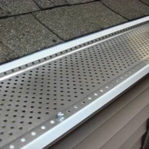 Close-up view of a Shur FLO 5-inch gutter guard installed on a residential gutter, showing its perforated aluminum surface designed to block leaves and debris while allowing rainwater to flow freely.