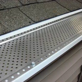 Close-up view of a Shur FLO 5-inch gutter guard installed on a residential gutter, showing its perforated aluminum surface designed to block leaves and debris while allowing rainwater to flow freely.