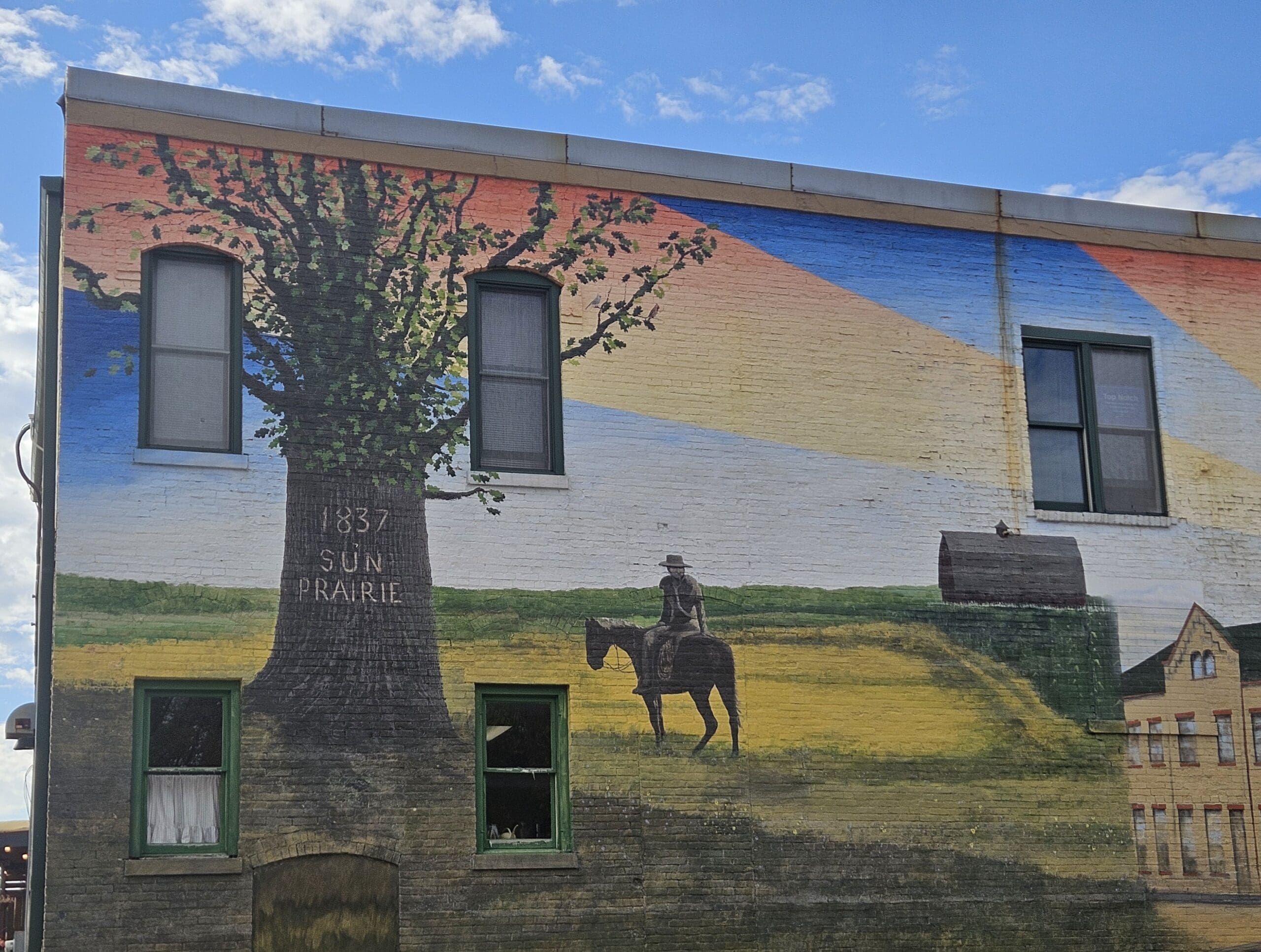 Mural in Sun Prairie, WI showing a tree with ‘1837 Sun Prairie’ and a horseback rider, highlighting the area where Modern Exterior provides expert roof replacement and repair services.