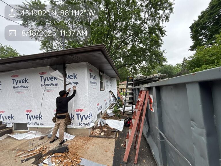 Worker wrapping Menomonee Falls home in Tyvek underlayment during vinyl siding installation by Modern Exterior