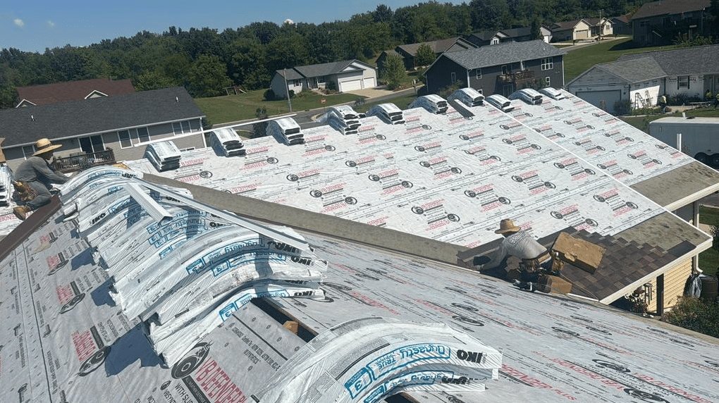 Roofing crew installing asphalt shingles over underlayment and ice and water shield during roof replacement.