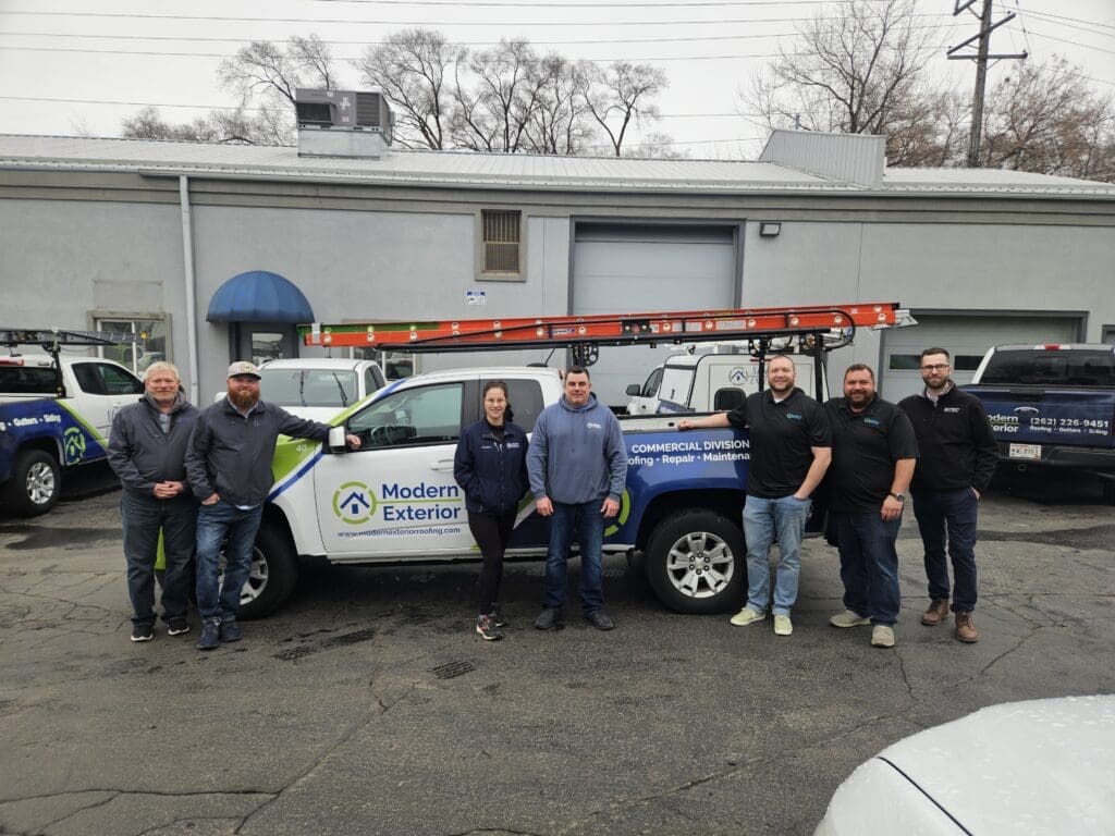 Modern Exterior commercial roofing team standing with a company truck in the office parking lot.