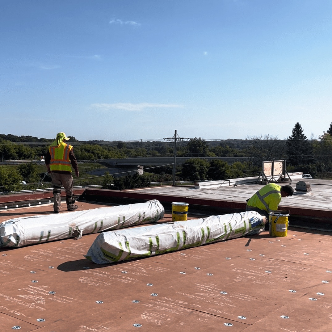 Modern Exterior crew preparing flat roof with insulation board and membrane rolls before installation on commercial building