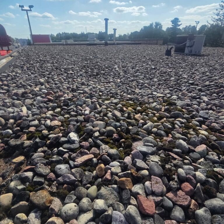Gravel-covered flat commercial roof at Take 5 in Wisconsin Rapids before PVC roof replacement, showing existing rock ballast and rooftop equipment
